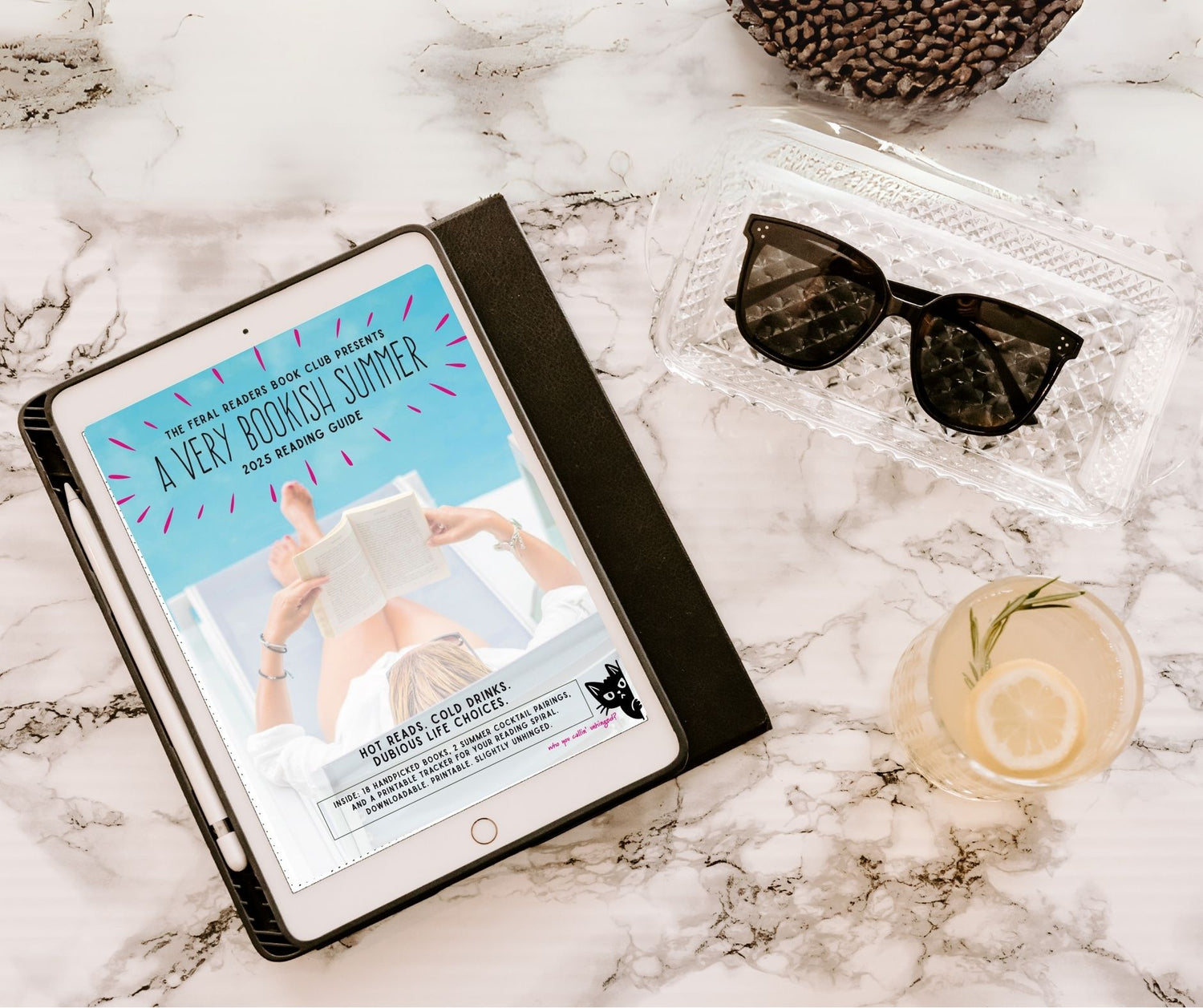 Tablet displaying a book club guide on a marble surface with sunglasses and a drink.